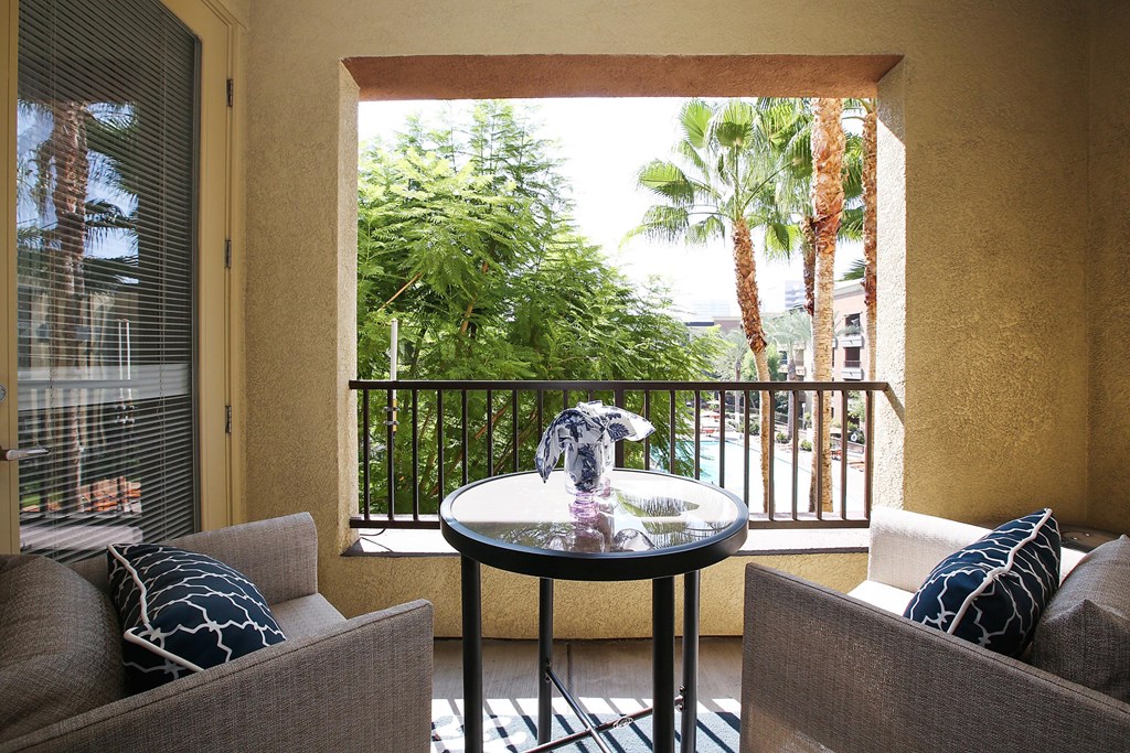 A balcony with a table and two chairs overlooking a lush green area at The Kitt at Warner Center Apartments, California