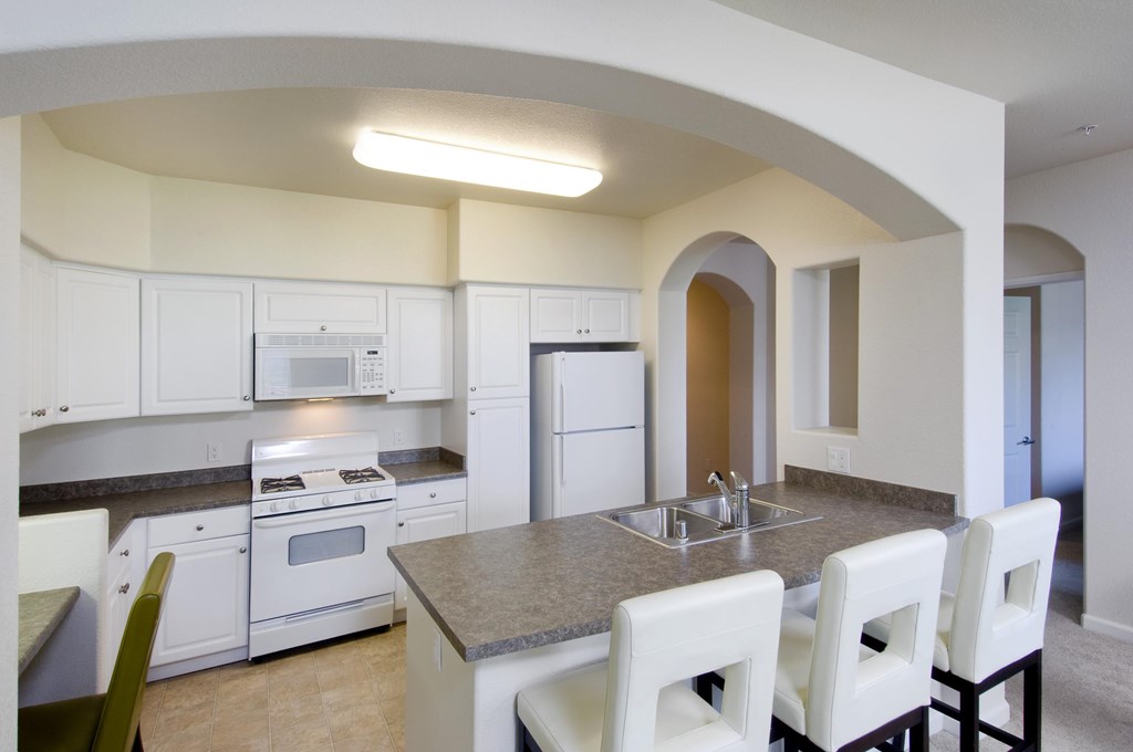 A kitchen with white cabinets and a countertop with a sink and four chairs at The Kitt at Warner Center Apartments, California