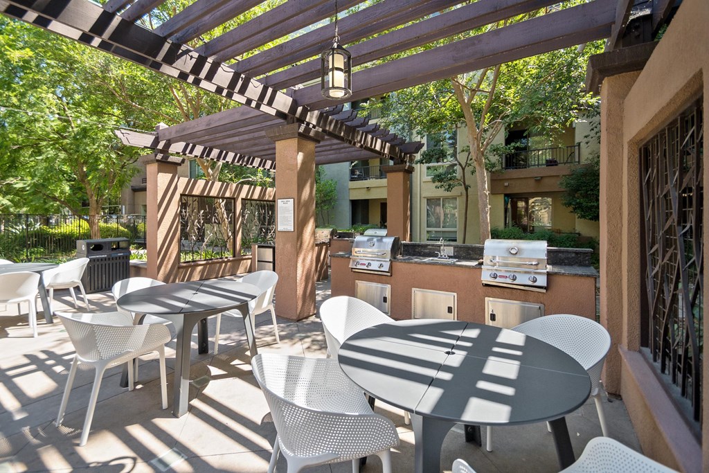 A patio with white chairs and tables is covered by a striped awning at The Kitt at Warner Center Apartments, Woodland Hills, CA, 91303