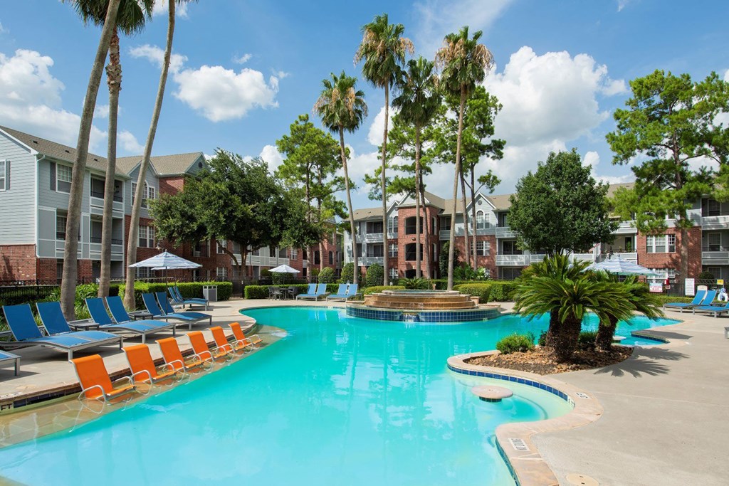 a large swimming pool with orange chairs in front of apartment buildings at Veranda at Centerfield, Texas