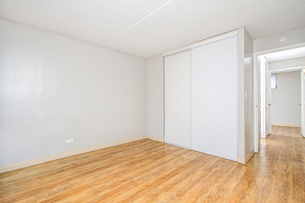 the living room and bedroom of an apartment with wood floors and white walls at Waikele Towers Apartments, Waipahu