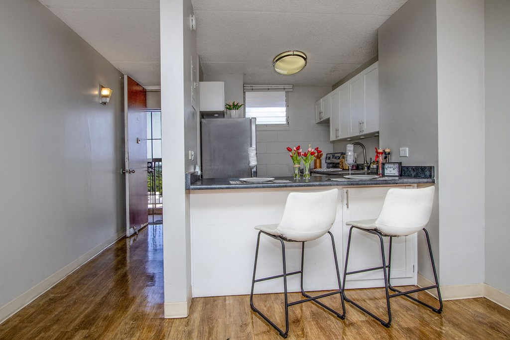 a kitchen with white cabinets and a counter with two white chairs at Waikele Towers Apartments, Waipahu, 96797