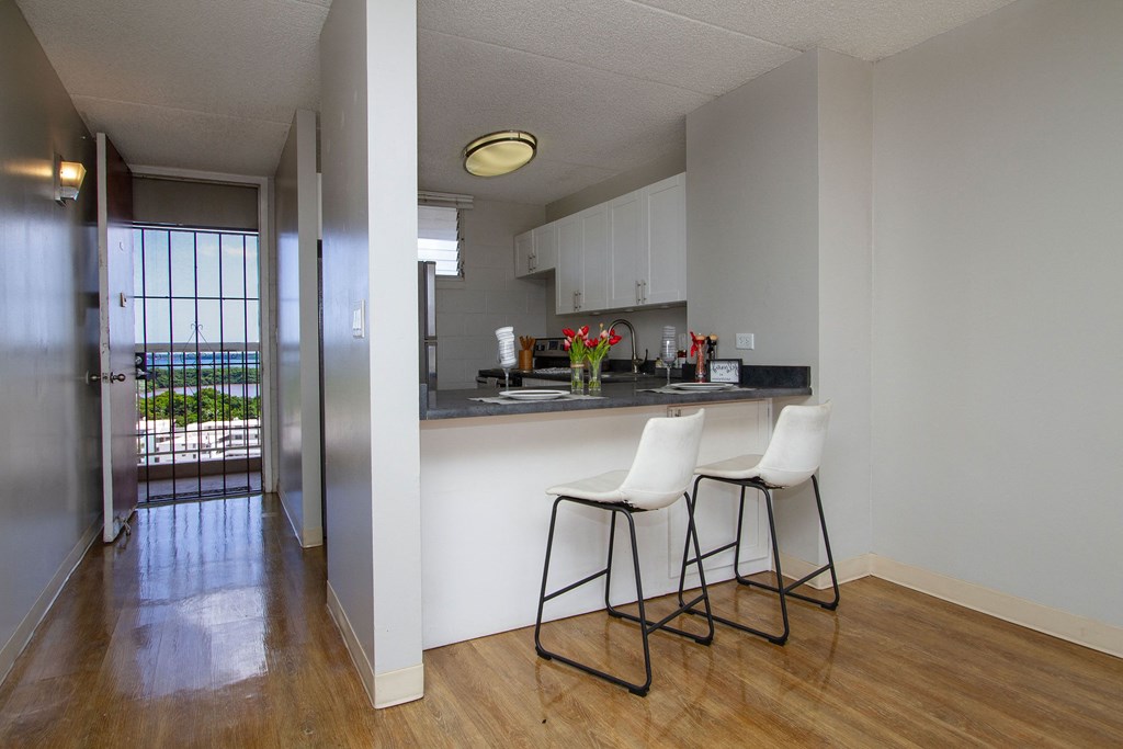 a view of a kitchen with two stools in front of a bar with chairs at Waikele Towers Apartments, Waipahu, HI