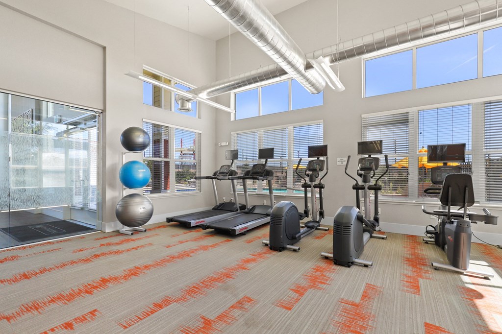 a gym with weights and exercise equipment in a building with large windows at Ridge at Thornton Station Apartments, Thornton, CO
