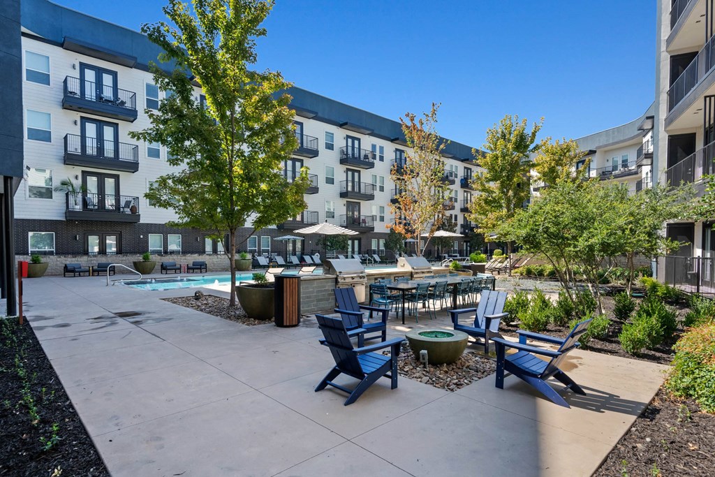 an outdoor patio with blue chairs and tables and an apartment building in the background at Abstract at Design District, Dallas, TX, 75207