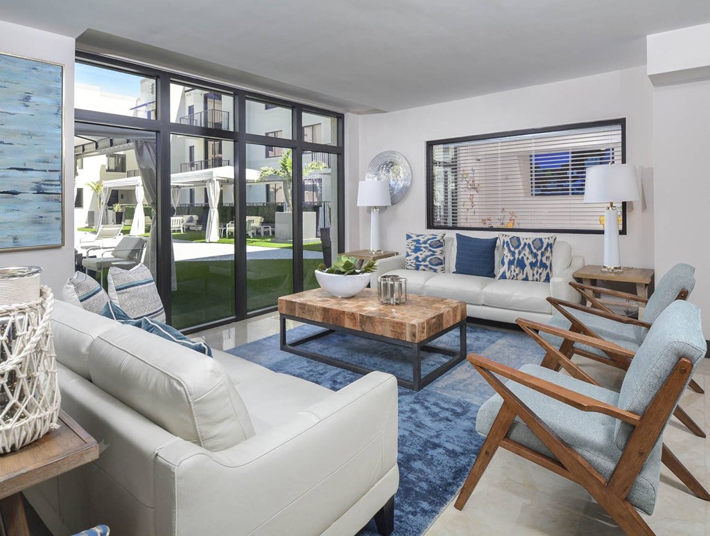 a living room with white couches and chairs and large windows at District West Gables, West Miami, Florida 33155