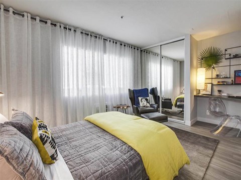 Modern bedroom with yellow accent bedding and seating area at Duet on Wilcox Apartments, Los Angeles