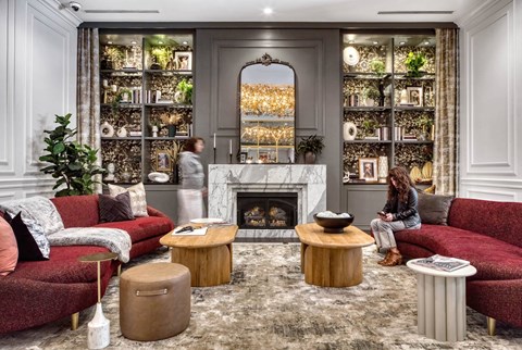 A woman is sitting on a red couch in a living room with a fireplace and shelves filled with plants.