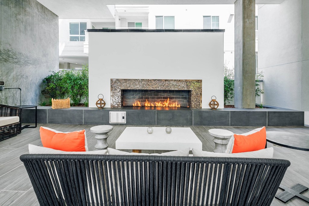 Outdoor dining area with a black chair in front of a fireplace at G12 Apartments in Los Angeles, CA