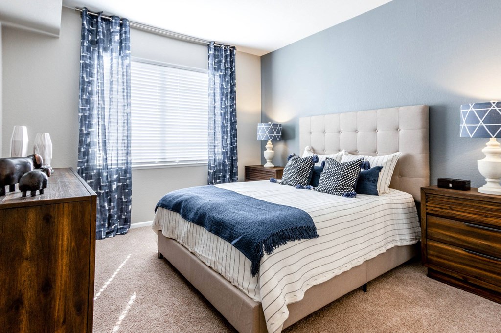 a bedroom with a bed and a window with blue curtains at The links at Plum Creek Apartments, Castlerock Colorado