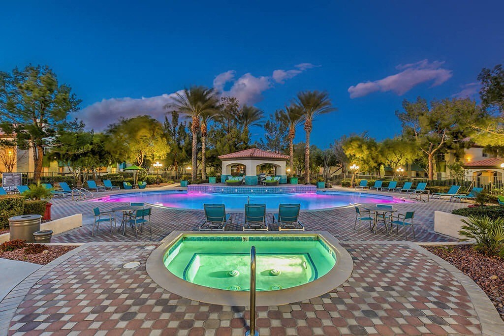 a large swimming pool with chairs and a jacuzzi at night at Mirasol Apartments, Las Vegas, NV