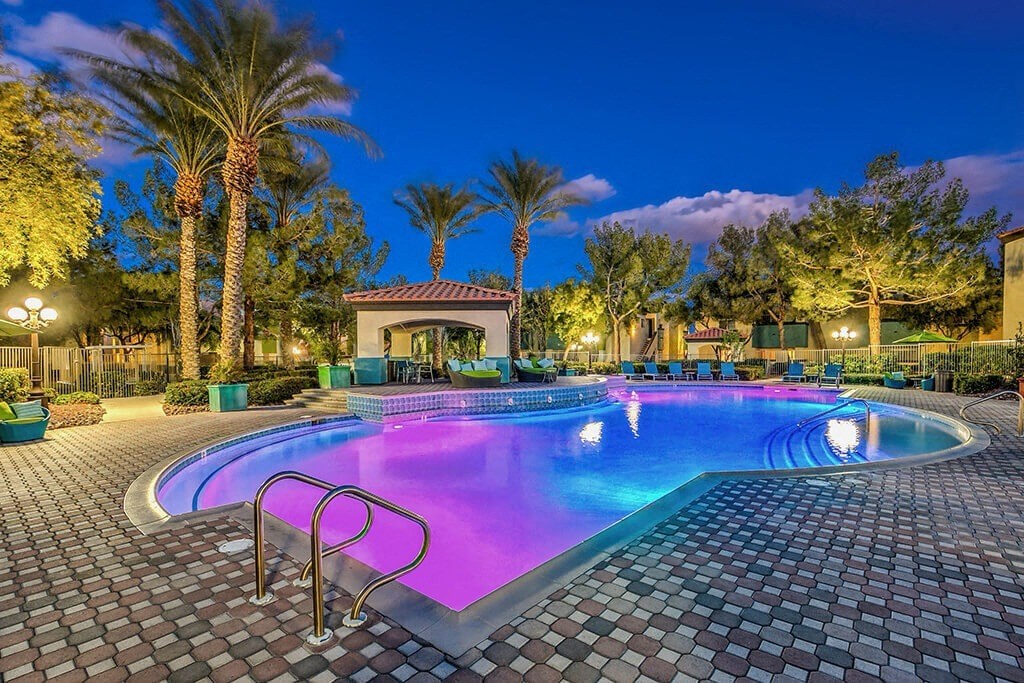 a large swimming pool at night with palm trees at Mirasol Apartments, Las Vegas