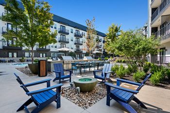 A sunny day at a courtyard with blue chairs and a fire pit at Abstract at Design District in Dallas, TX