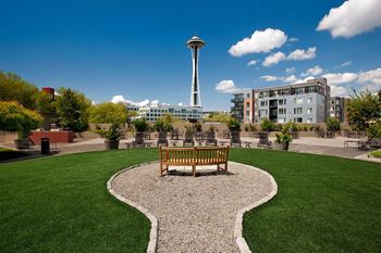 A park with a bench and a gravel pathway in the foreground and a tall tower in the background at Skye at Belltown Apartments, Seattle, WA