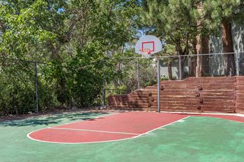 A basketball court with a red and green surface surrounded by a fence and trees. at Arcadia Apartments, CO