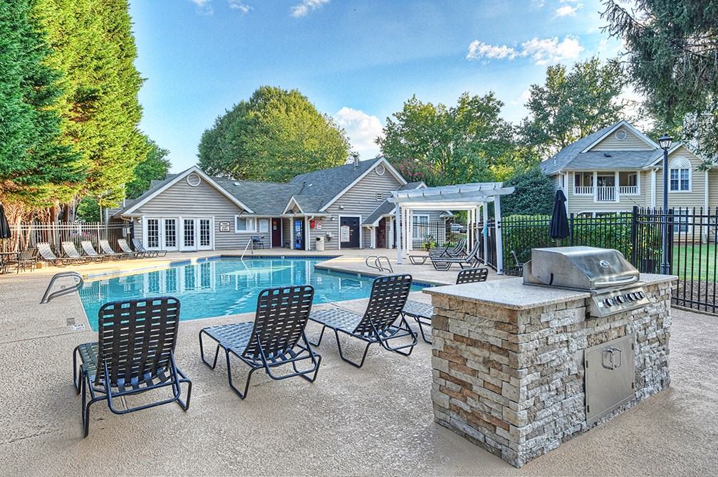 a pool with patio furniture and a grill in front of a house
