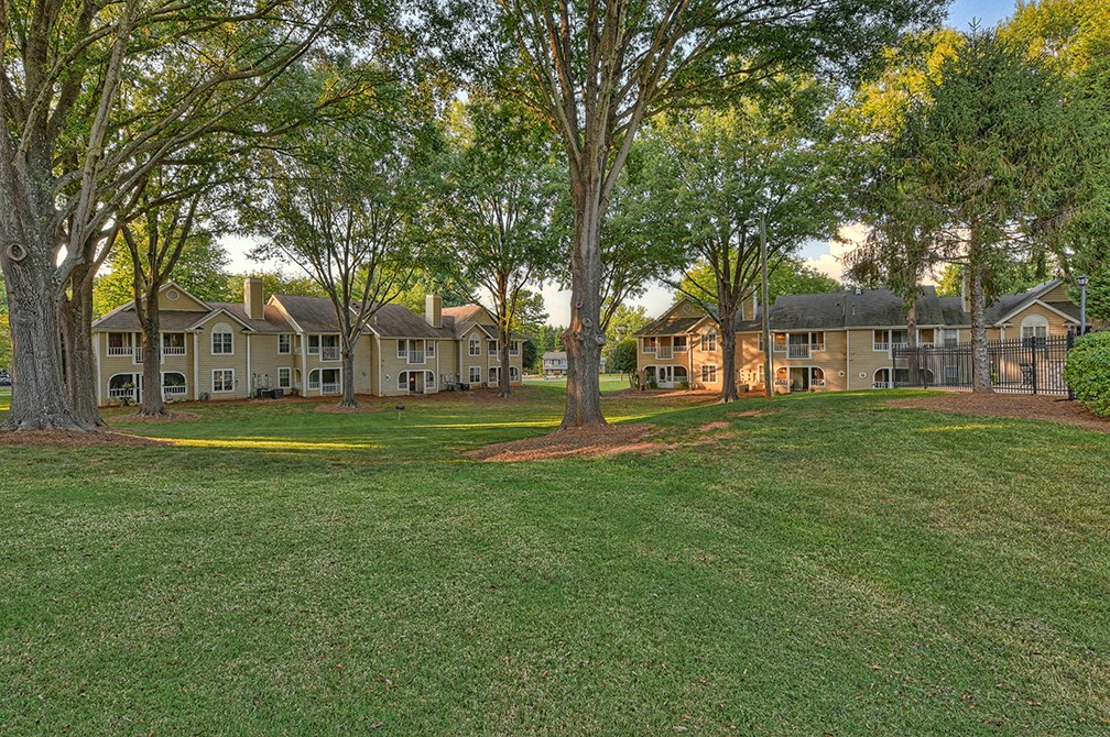 a large grassy area with trees in front of some apartments