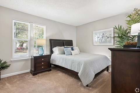 A bedroom with a bed, nightstand, and a plant.
