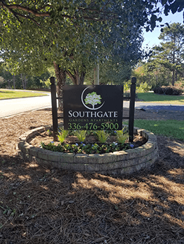 A sign for Southgate Gardens is surrounded by plants and a tree.
