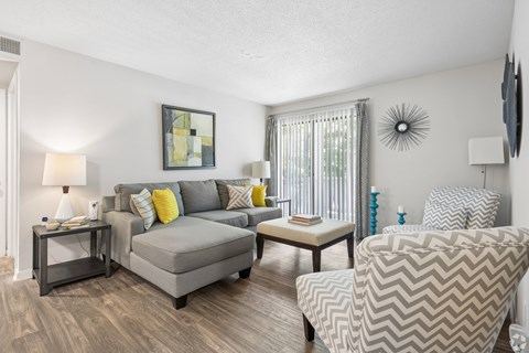 A living room with a grey couch, a grey armchair, and a small table with a lamp on it.