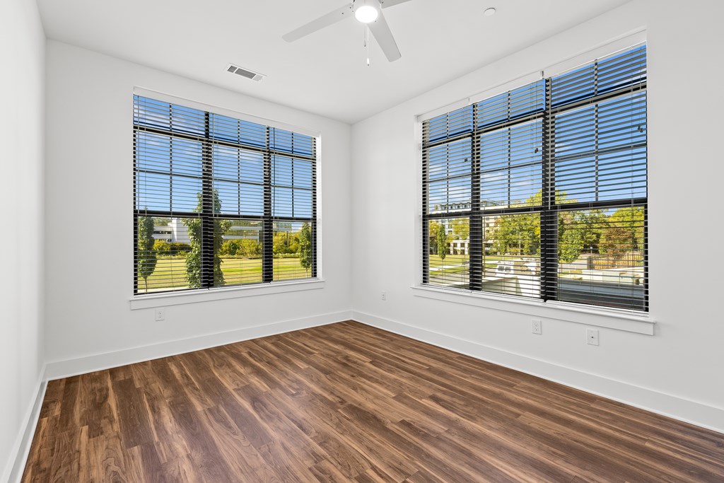 A room with wooden floors and two windows with blinds.