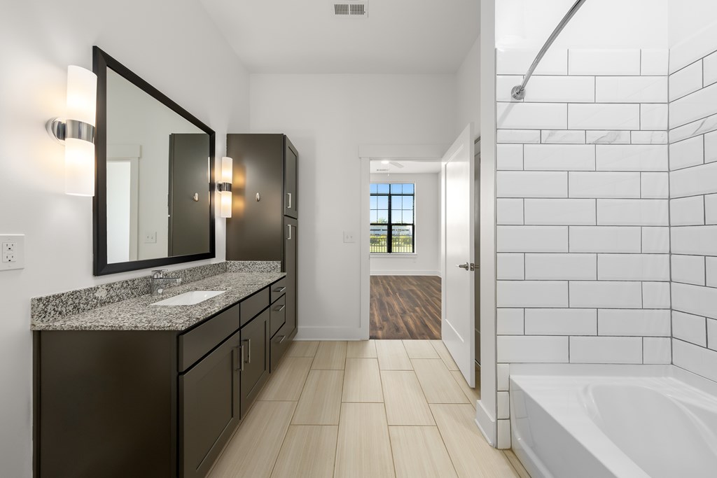 A bathroom with a white tub and a sink with a granite counter.