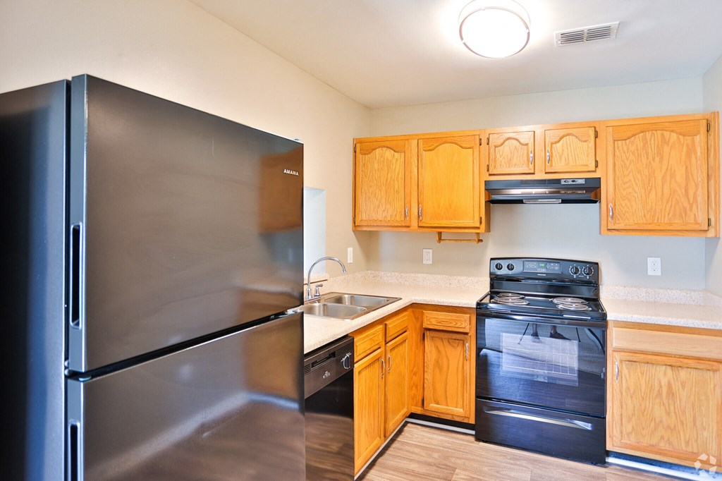 A kitchen with a black refrigerator and wooden cabinets.