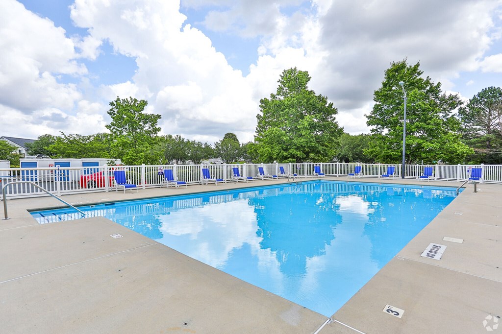 A large outdoor swimming pool surrounded by trees and a fence.