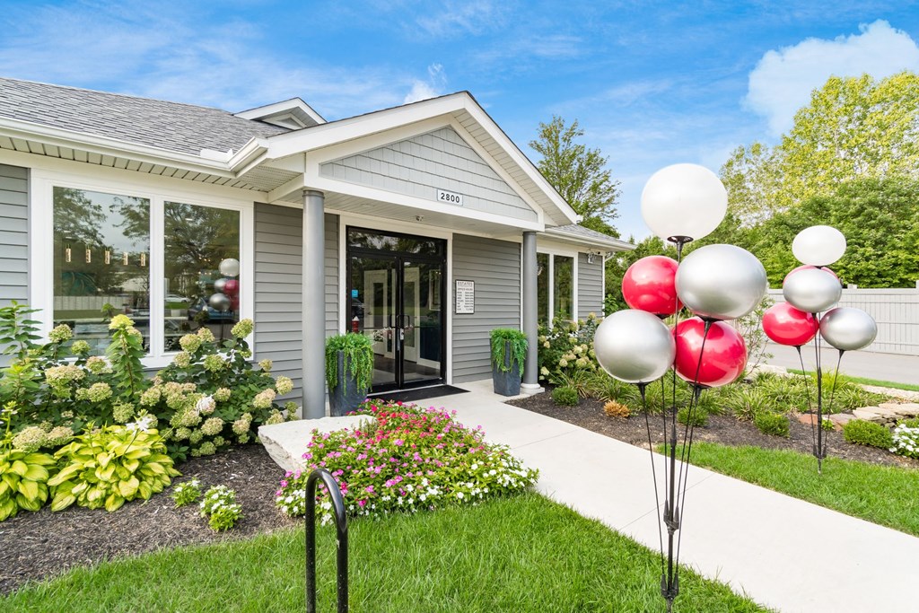 A house with a grey siding and a white door is surrounded by a garden with red and white balloons. at Estates at Brentwood Lake Apartments, Reynoldsburg, OH, 43068