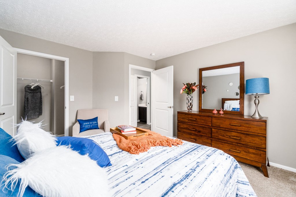 A bedroom with a bed, dresser, mirror, and lamp. at Estates at Brentwood Lake Apartments, Ohio
