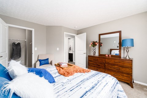 A bedroom with a bed, dresser, mirror, and lamp. at Estates at Brentwood Lake Apartments, Ohio