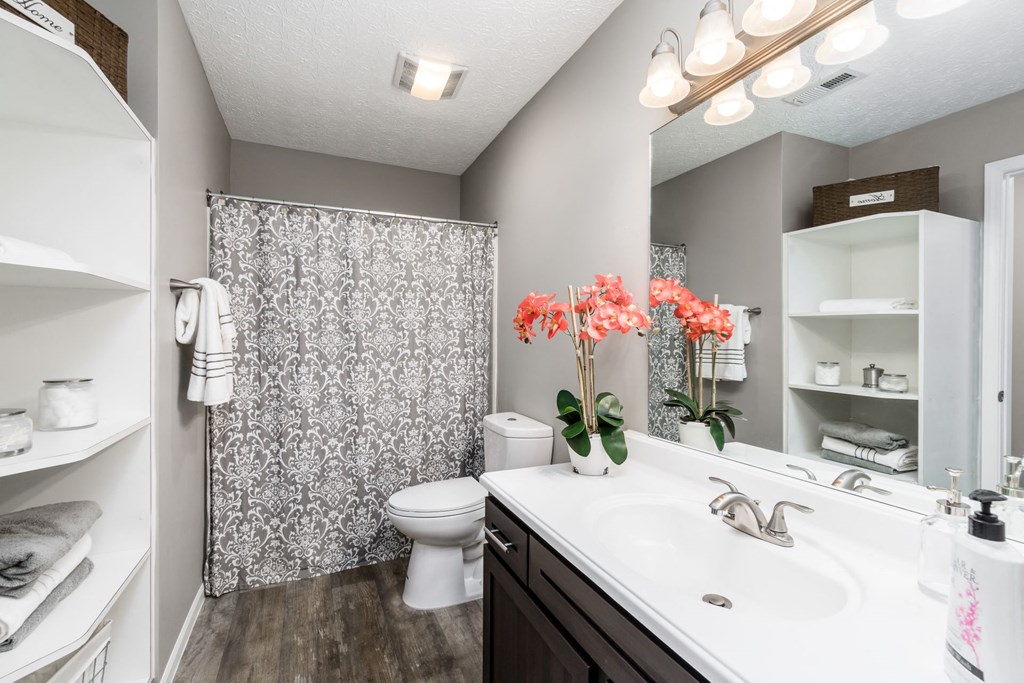 A bathroom with a white sink, toilet, and a shower with a grey and white shower curtain at Estates at Brentwood Lake Apartments, Reynoldsburg