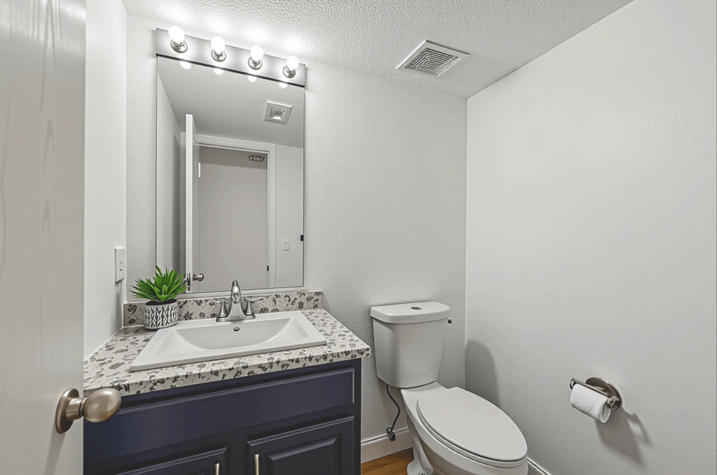 A bathroom with a sink, mirror, toilet and lights on the mirror.