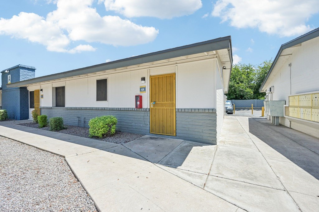 A building with a yellow door is surrounded by a gravel area and a concrete walkway.