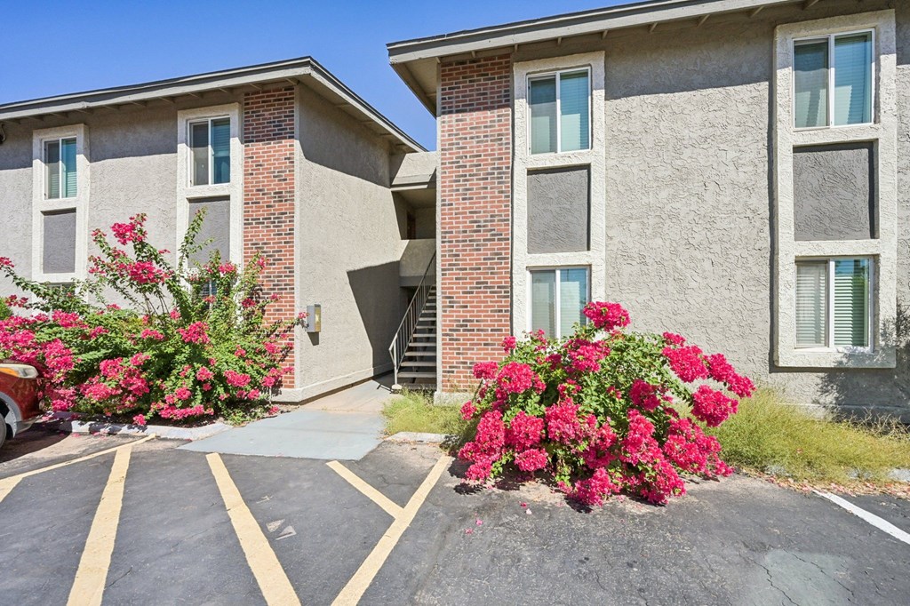A red car is parked in a parking lot in front of a building.