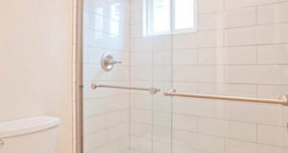A white tiled bathroom with a toilet and a shower.