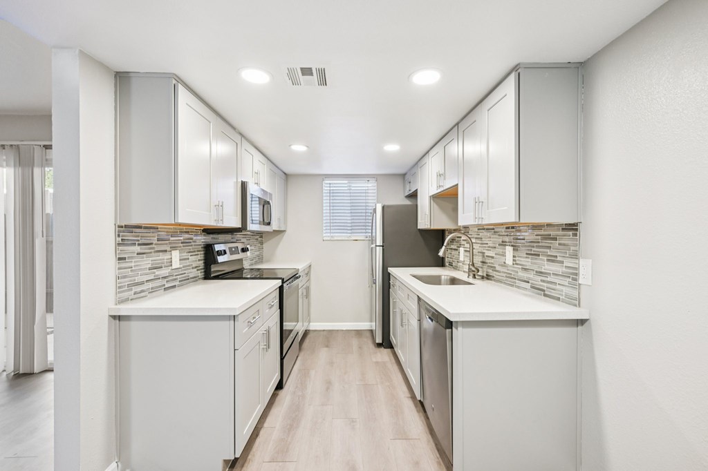 A modern kitchen with white cabinets and a wooden floor.