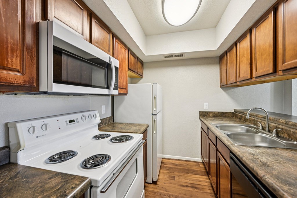 A kitchen with a white stove top oven, a microwave above it, a white refrigerator, and a granite counter top.