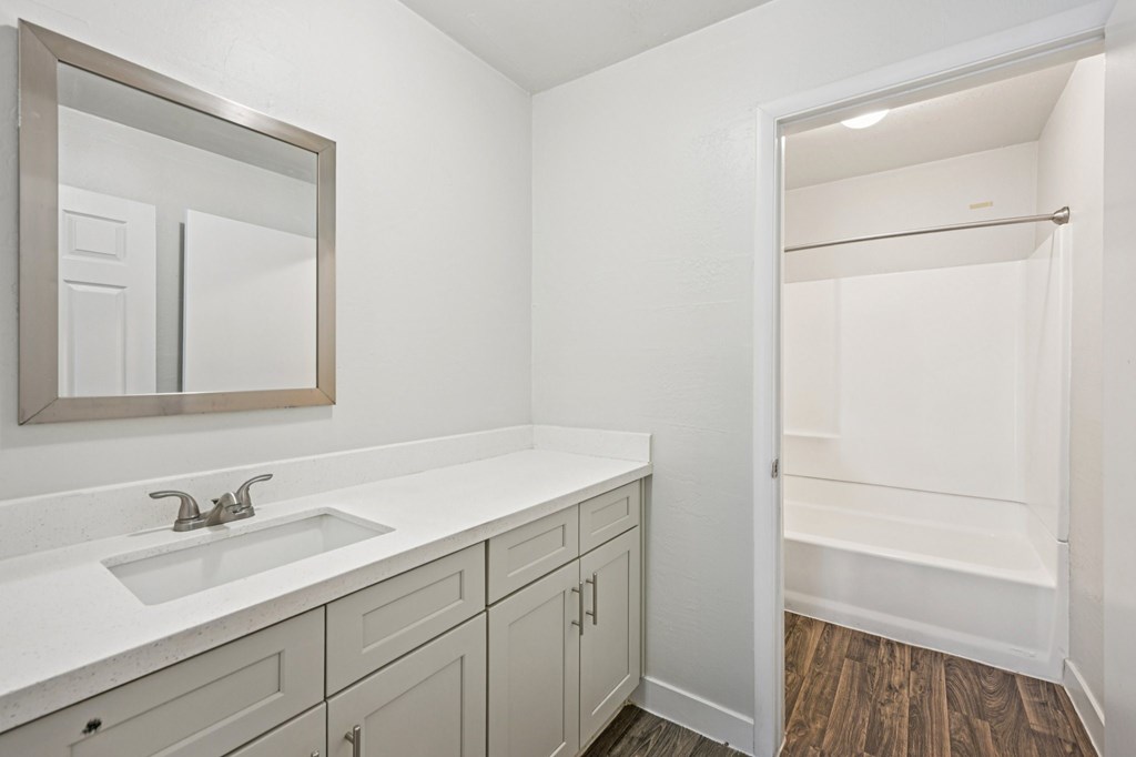 A bathroom with a sink, mirror, and wooden floor.