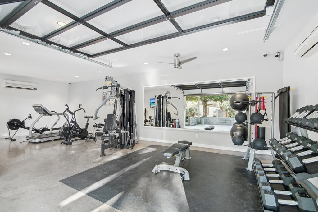 A spacious home gym with a variety of equipment including a treadmill, weights, and a bench. at The Viridian Apartments, Arizona
