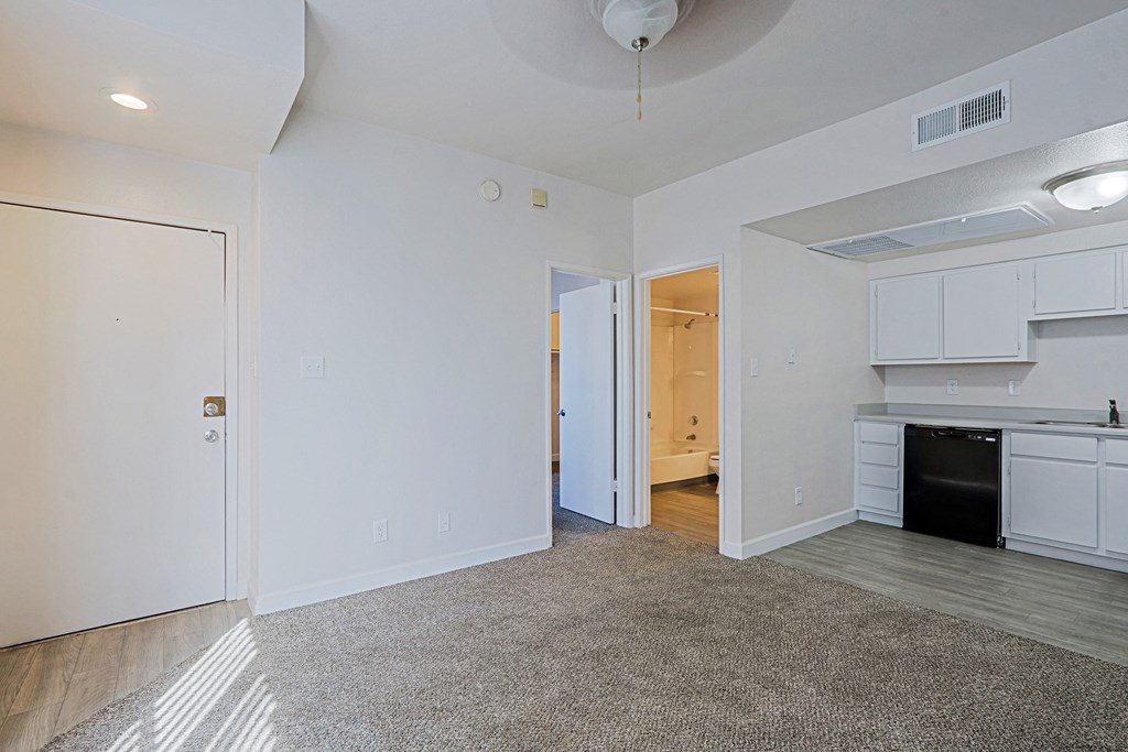 the living room and kitchen of an apartment with white walls and wood flooring