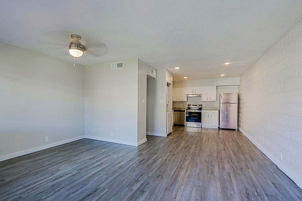 A kitchen with white cabinets and a refrigerator is visible through an open door in a room with wooden floors.
