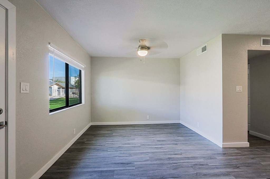 A spacious room with a ceiling fan and a window overlooking a building.