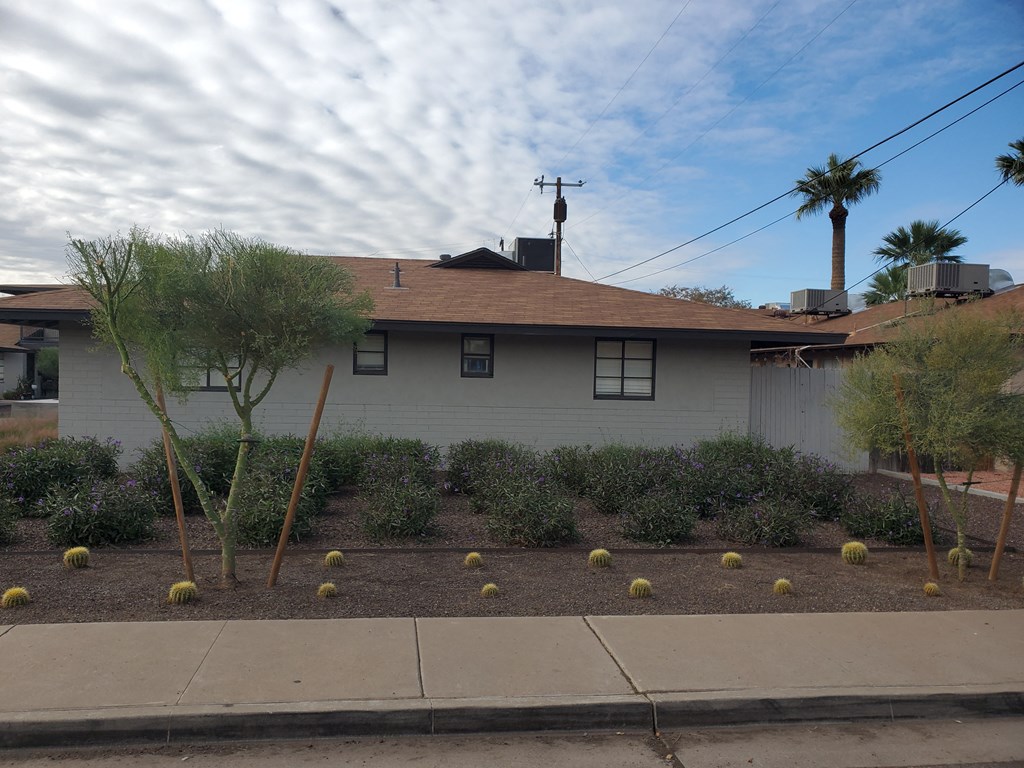 the front yard of a white house with a garden and trees