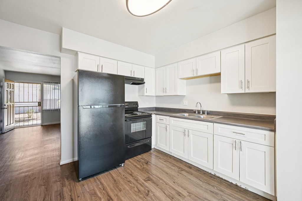 A black refrigerator is in a kitchen with white cabinets.