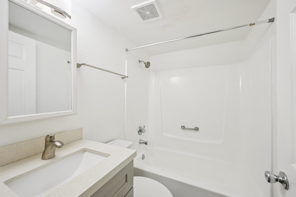 A white bathroom with a sink, mirror, and shower.