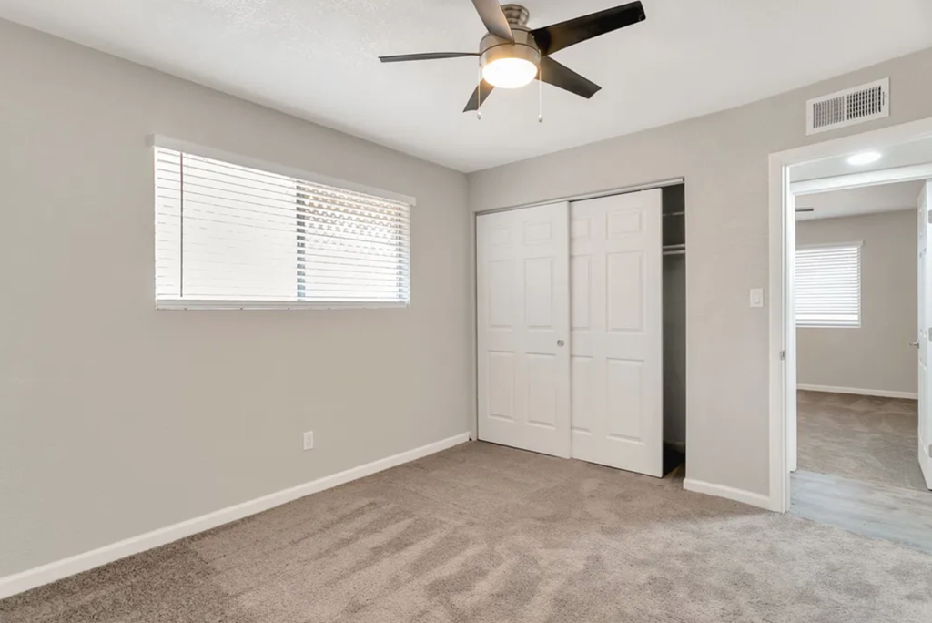 an empty living room with a ceiling fan and a closet
