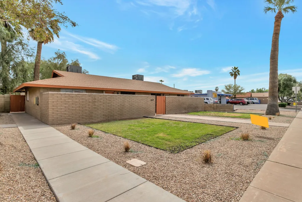 the front yard of a brick house with a lawn and a sidewalk