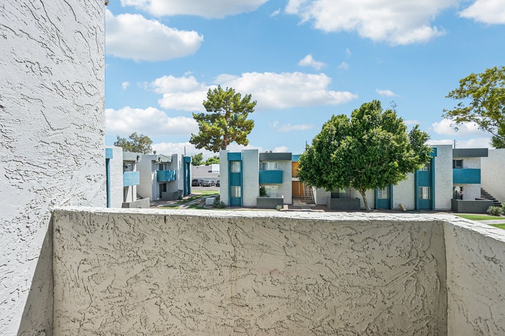 A white wall with a concrete ledge in the foreground and a row of blue buildings in the background.