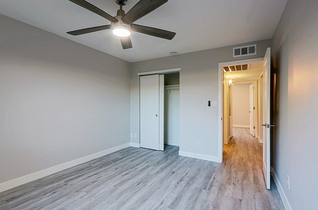 A room with a ceiling fan and light, two doors, and a wooden floor.